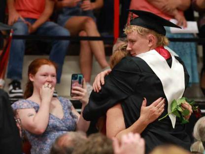 Micah Galvan hugs his mom, Heather McClendon, as Ambriana McClendon captures the moment on her phone. Seniors handed a rose to a significant adult near the start of commencement. Photos by KAREN BONAR/Ellsworth County Independent-Reporter